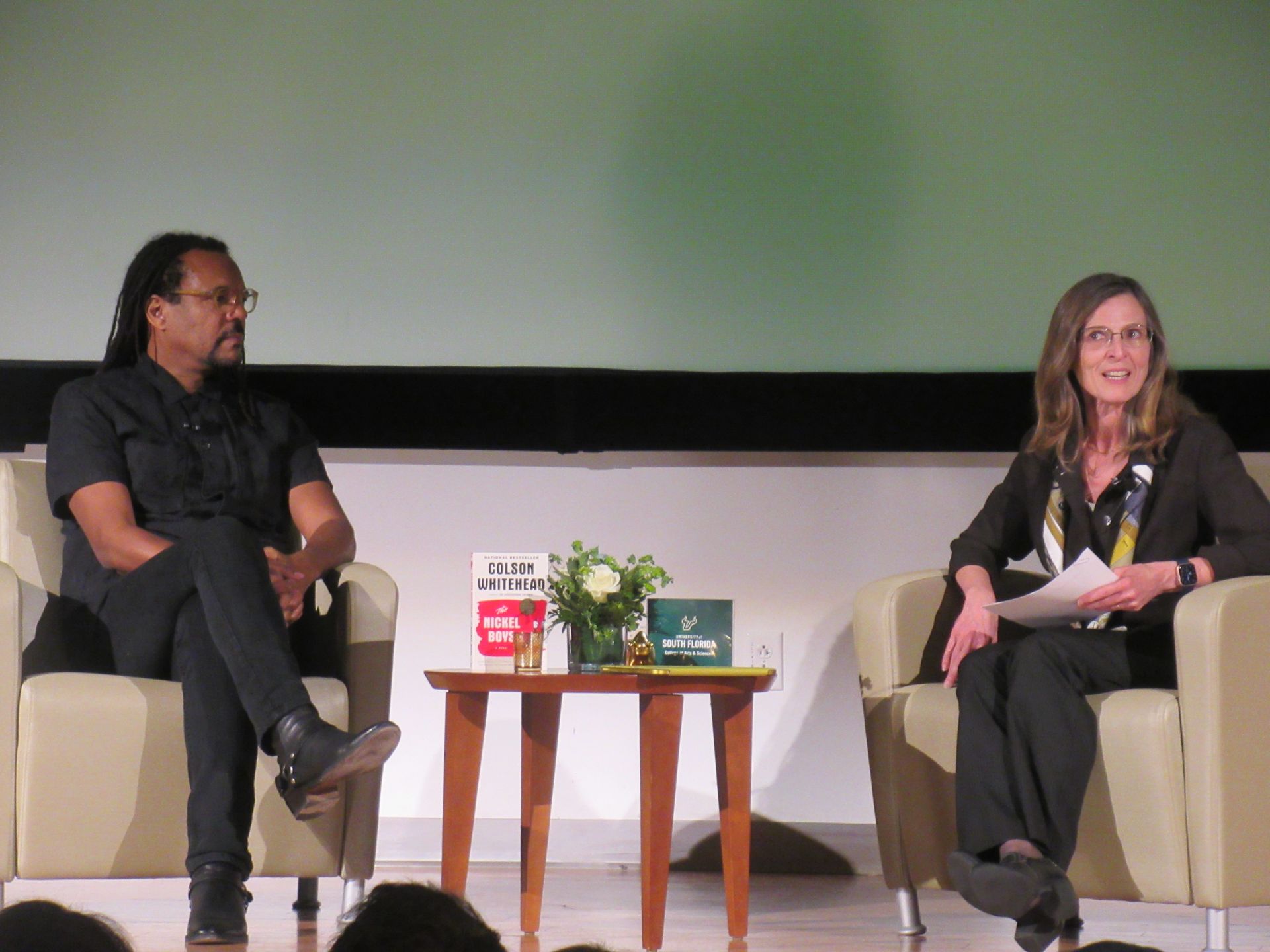 Two people on stage: a man with dreadlocks and a woman with glasses, in chairs, speaking.