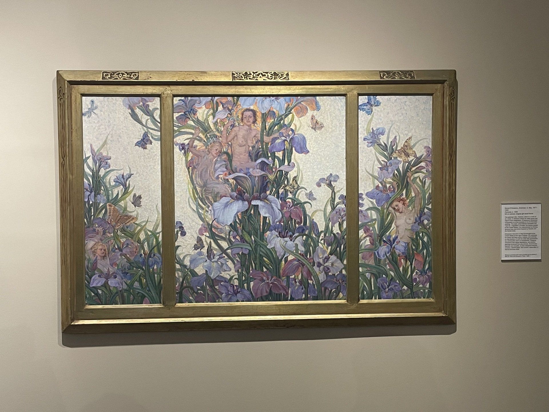 Painting of fairies amidst irises, framed in gold. Soft colors of purple, pink, and green.