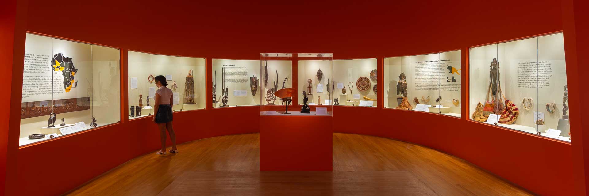 A museum exhibit with display cases, a woman looking at artifacts, and red walls.