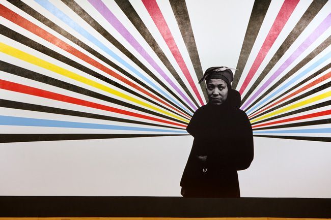 Woman in black coat against colorful striped background.
