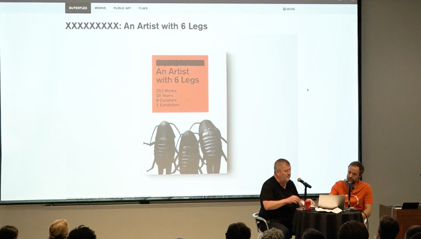 Two men presenting in front of a screen displaying a book cover: