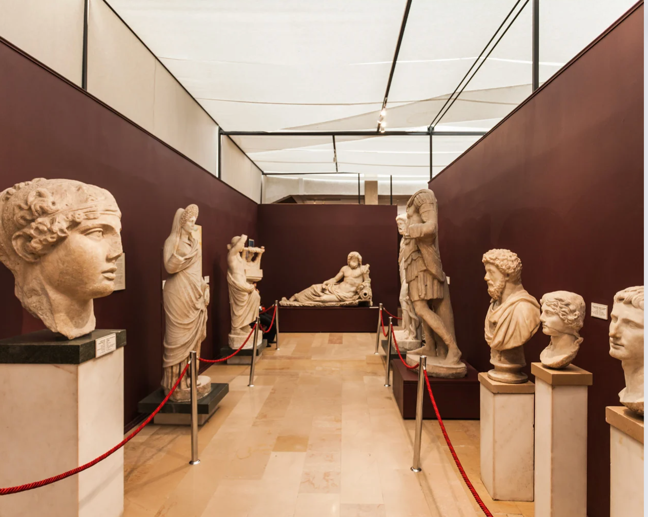 Museum exhibit with Roman sculptures on pedestals along a hallway with burgundy walls and a white ceiling.