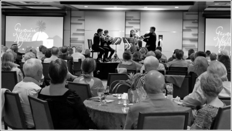 Black and white photo: Musicians performing for an audience in a banquet room. People seated at round tables.