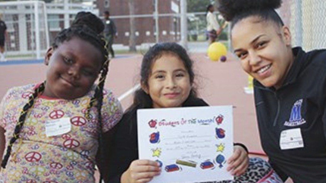 Three smiling people, one holding a certificate outdoors.
