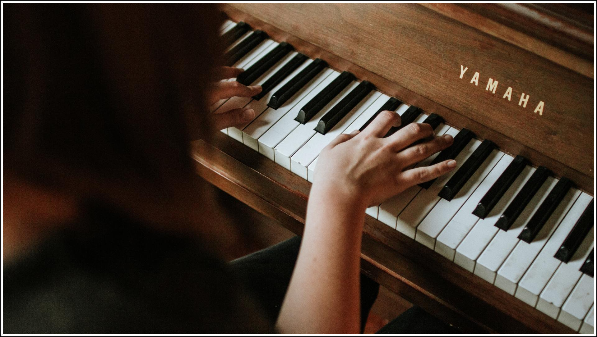 Person's hands playing a Yamaha piano with a brown wooden finish.