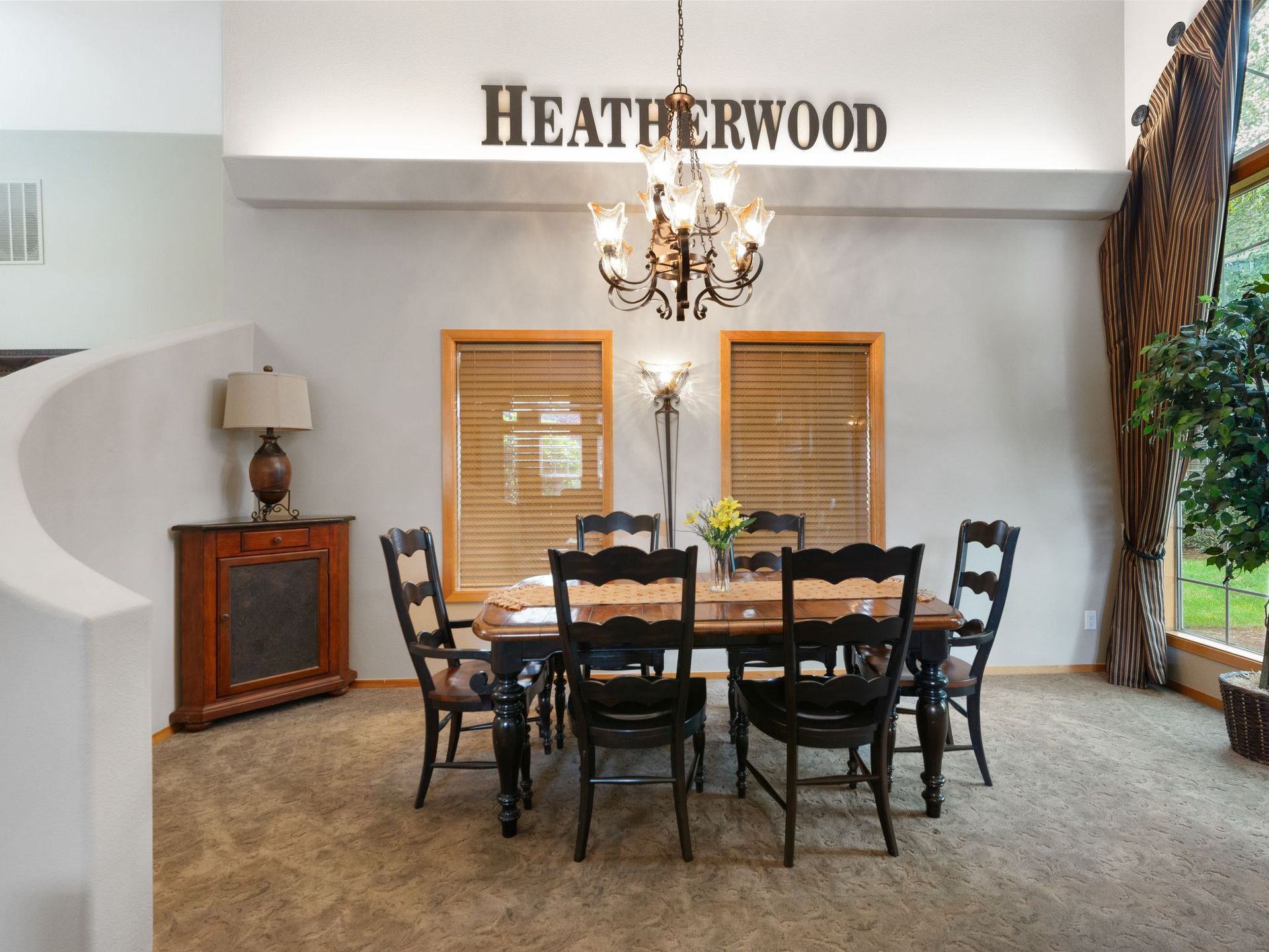 Dining room with dark wood table and chairs, chandelier, and windows under a “HEATHERWOOD” sign