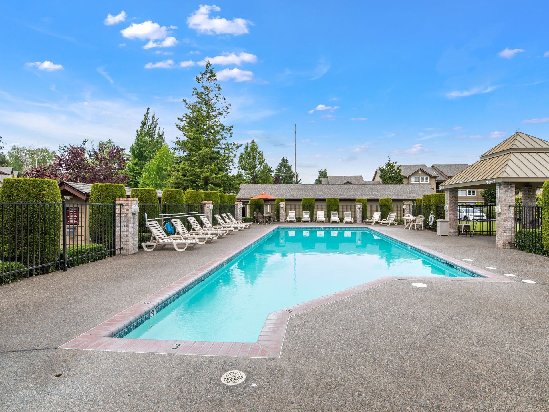 Outdoor swimming pool with turquoise water, lounge chairs, and a landscaped patio under a blue sky