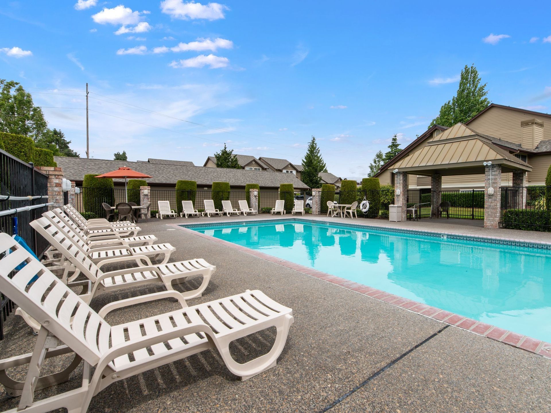 Outdoor pool with white lounge chairs, blue water, and a covered cabana under a clear sky