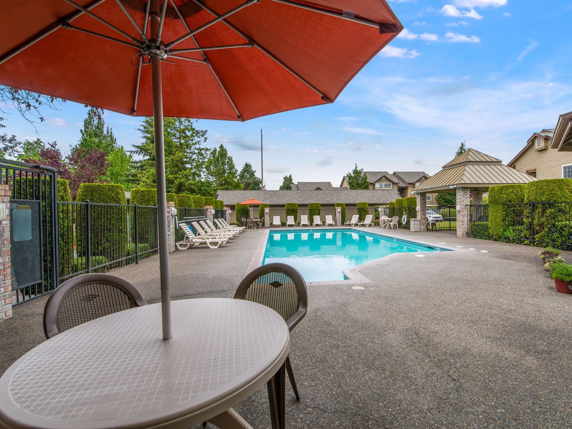 Patio table with red umbrella overlooking a backyard swimming pool and lounge chairs