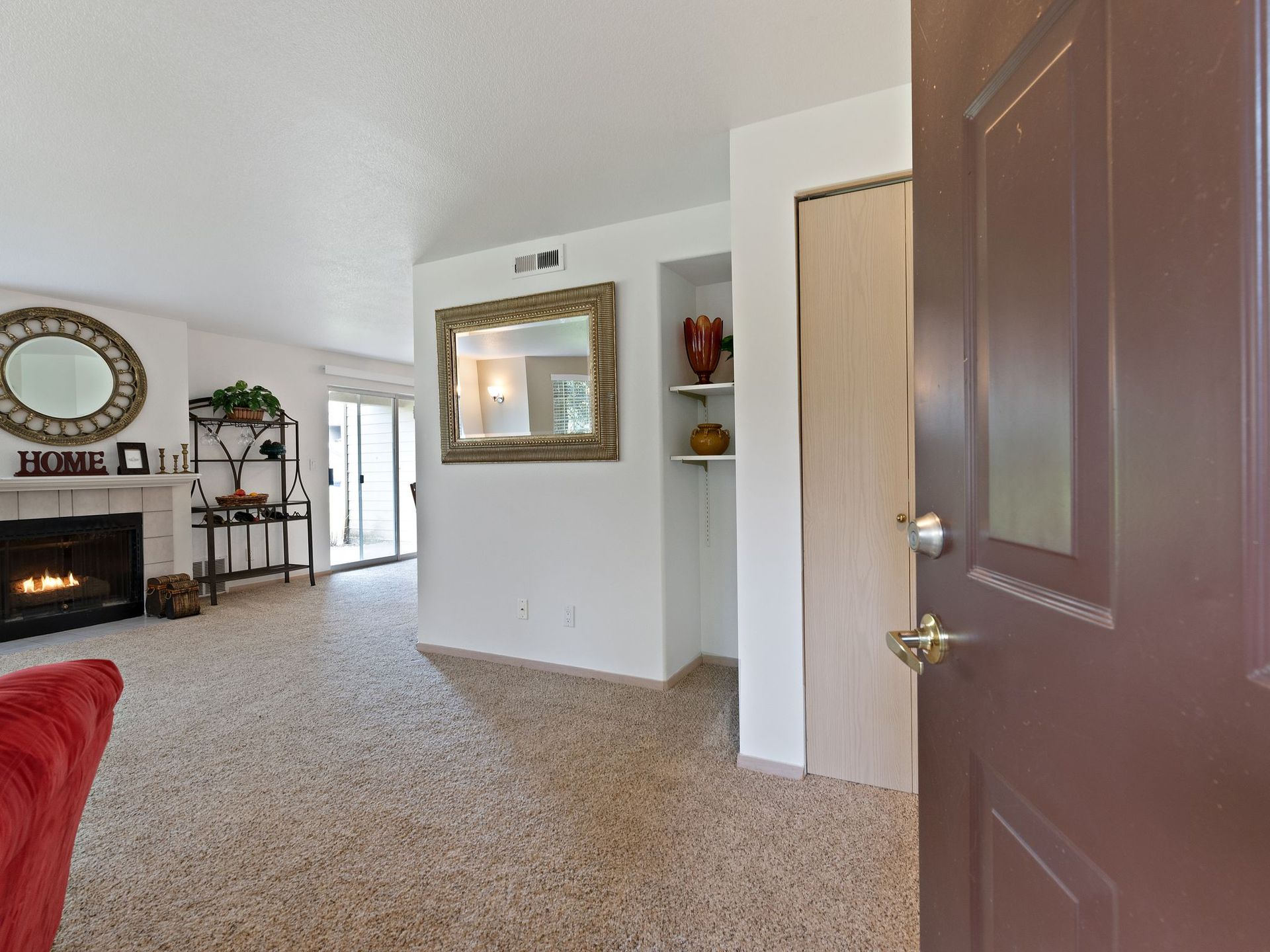 Living room with fireplace, mirror, carpeted floor, and an open front door visible on the right.