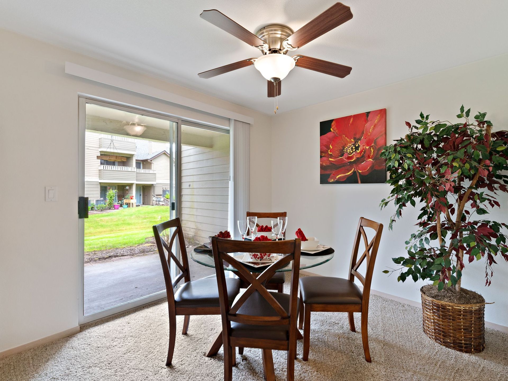 Dining nook with round table and chairs, ceiling fan, sliding door to patio, and potted tree by wall art