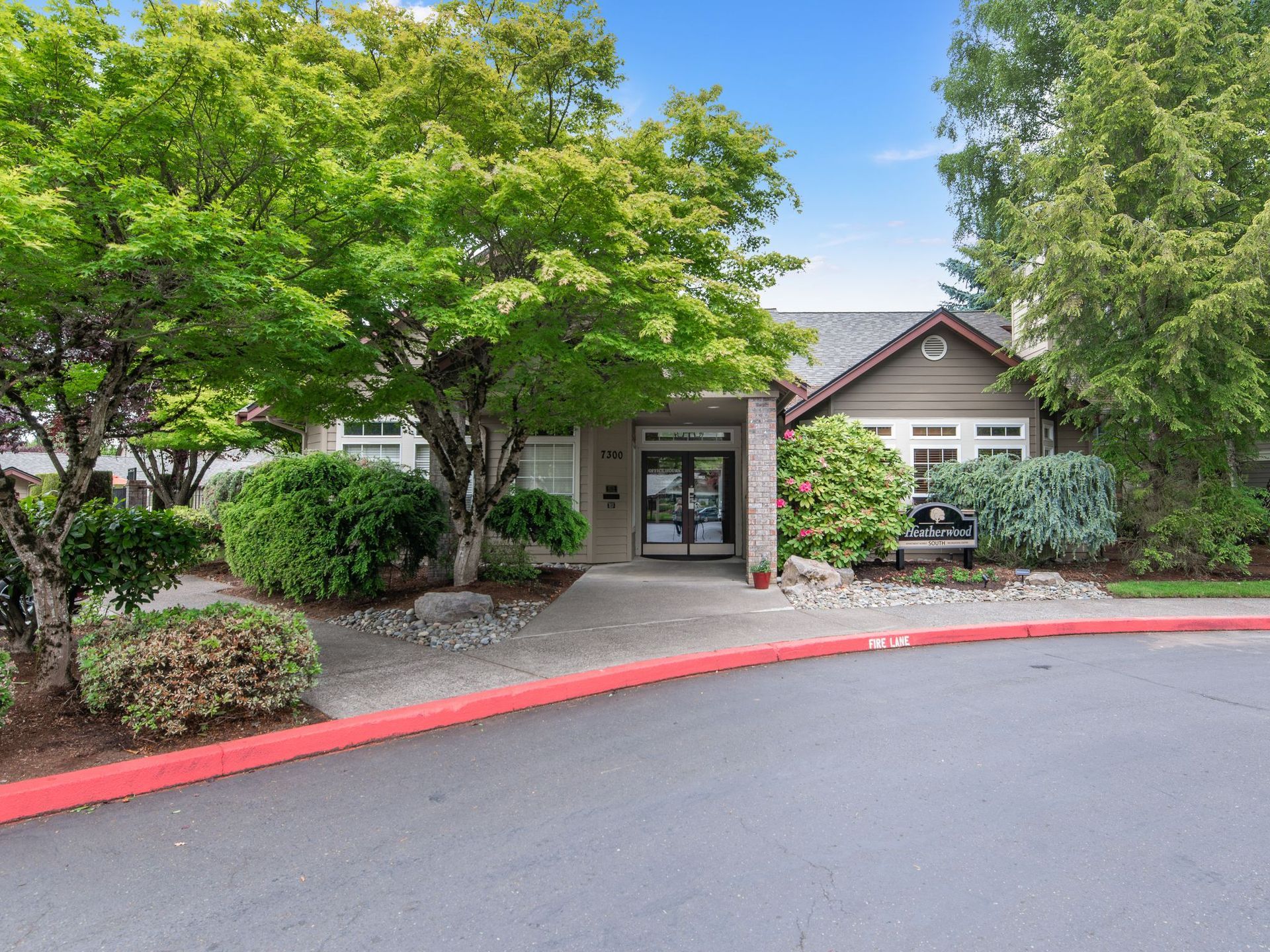Apartment building entrance with trees, shrubs, and a curved red curb in front