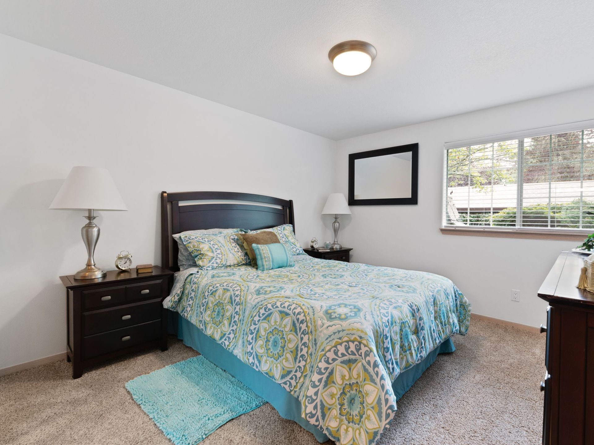 Bright bedroom with bed, blue patterned bedding, nightstands, window, and carpeted floor