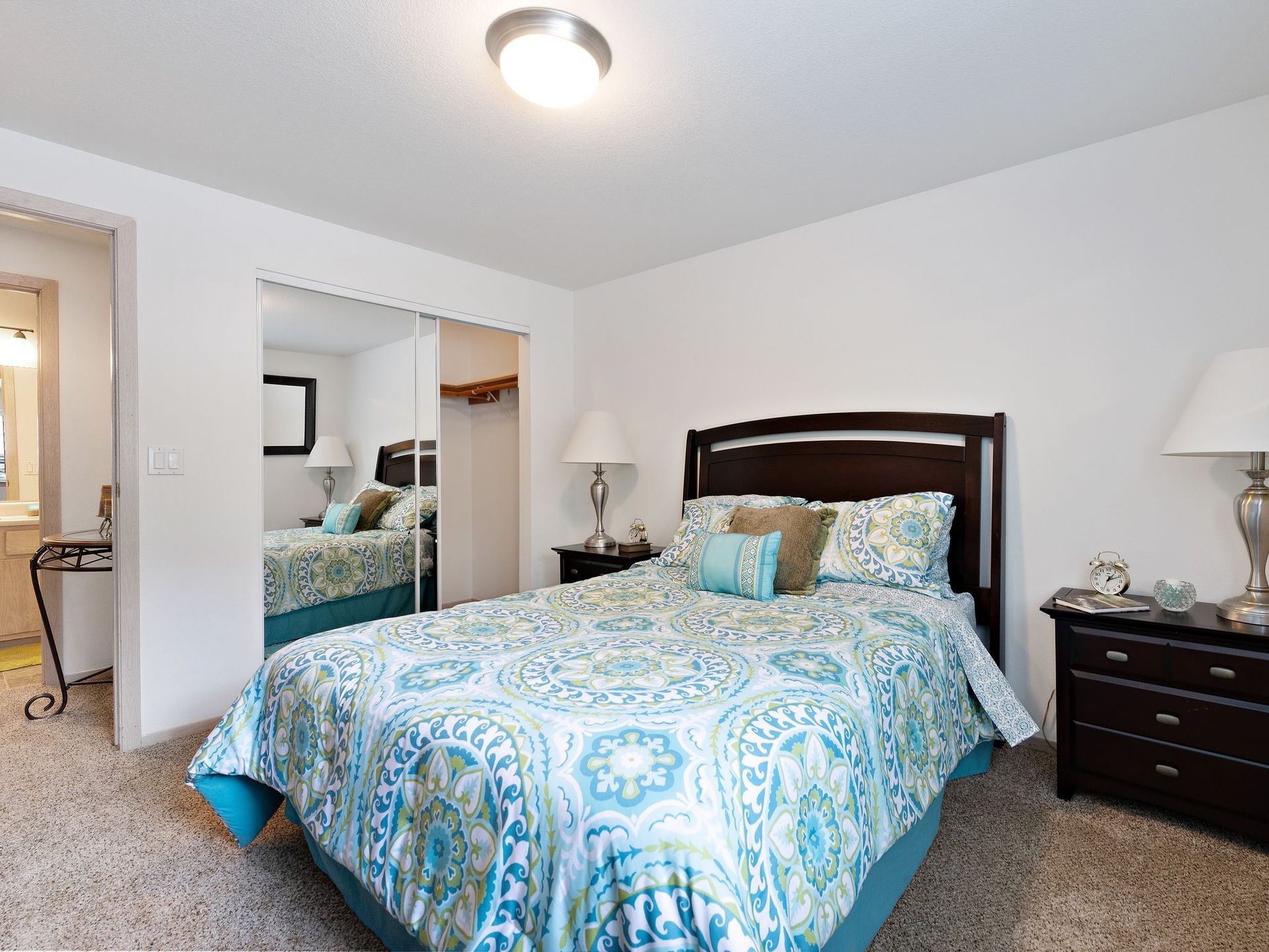 Bedroom with a dark wood bed, blue patterned bedding, and matching nightstands in a softly lit room