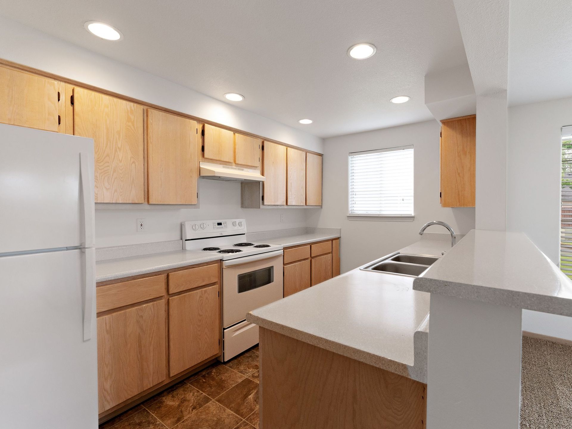 Bright, modern kitchen with white appliances, wood cabinets, and a large white island