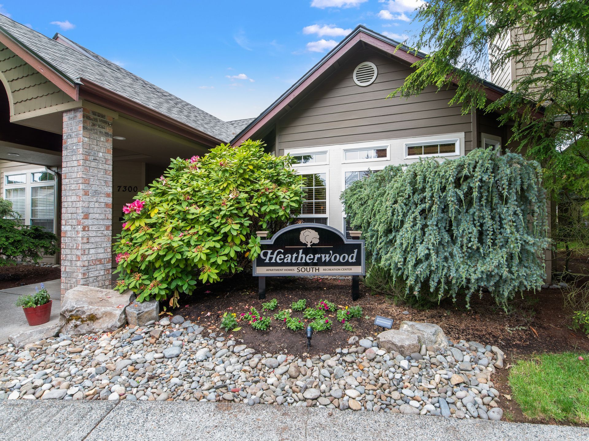 Suburban house entrance with a “Heatherwood” sign, brick columns, shrubs, and rock landscaping