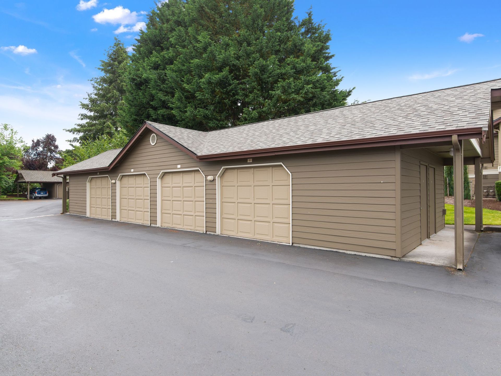 Row of beige garage doors beneath a gray shingled roof beside a paved driveway