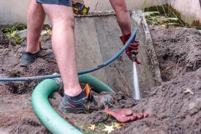Worker using a hose to spray water into a dirt trench at a construction site