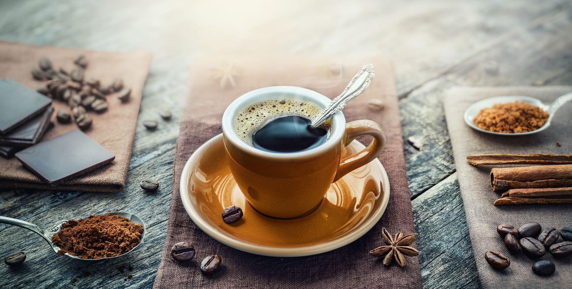 A cup of coffee with a spoon in it is on a saucer on a table.