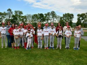 Group of people in white shirts and red bandanas standing together on a grassy field with trees behind them