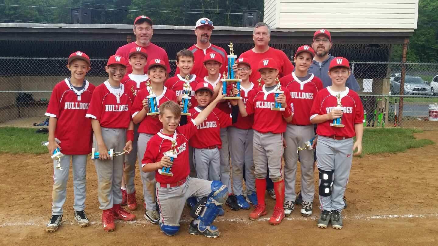 Youth baseball team in red uniforms posing with coaches on a dirt field after a game