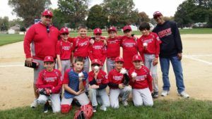 Youth baseball team in red uniforms posing together on a field with coaches