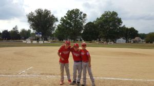 Three baseball players in red uniforms posing on a dusty field