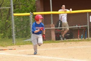 Young baseball player in a red helmet running past home plate on a dirt field