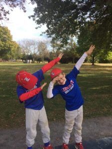Two children in red and blue clothes dab pose in a park on a sunny day