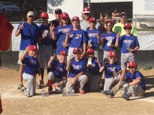 Youth baseball team in blue jerseys and red caps posing on a dirt field after a game.