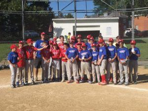 Baseball team posing on a field, wearing red and blue jerseys and caps in front of a chain-link fence.