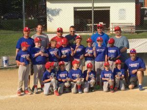 Youth baseball team and coaches posing on a field in blue and red uniforms.