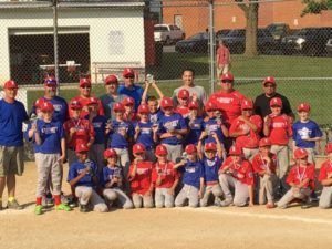Youth baseball teams in red and blue uniforms posing for a group photo on a field