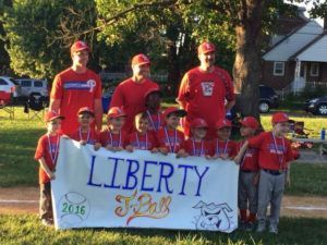 People in red shirts holding a “Liberty” sign during a daytime outdoor parade