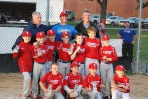 Youth baseball team in red uniforms posing with coaches on a field at dusk