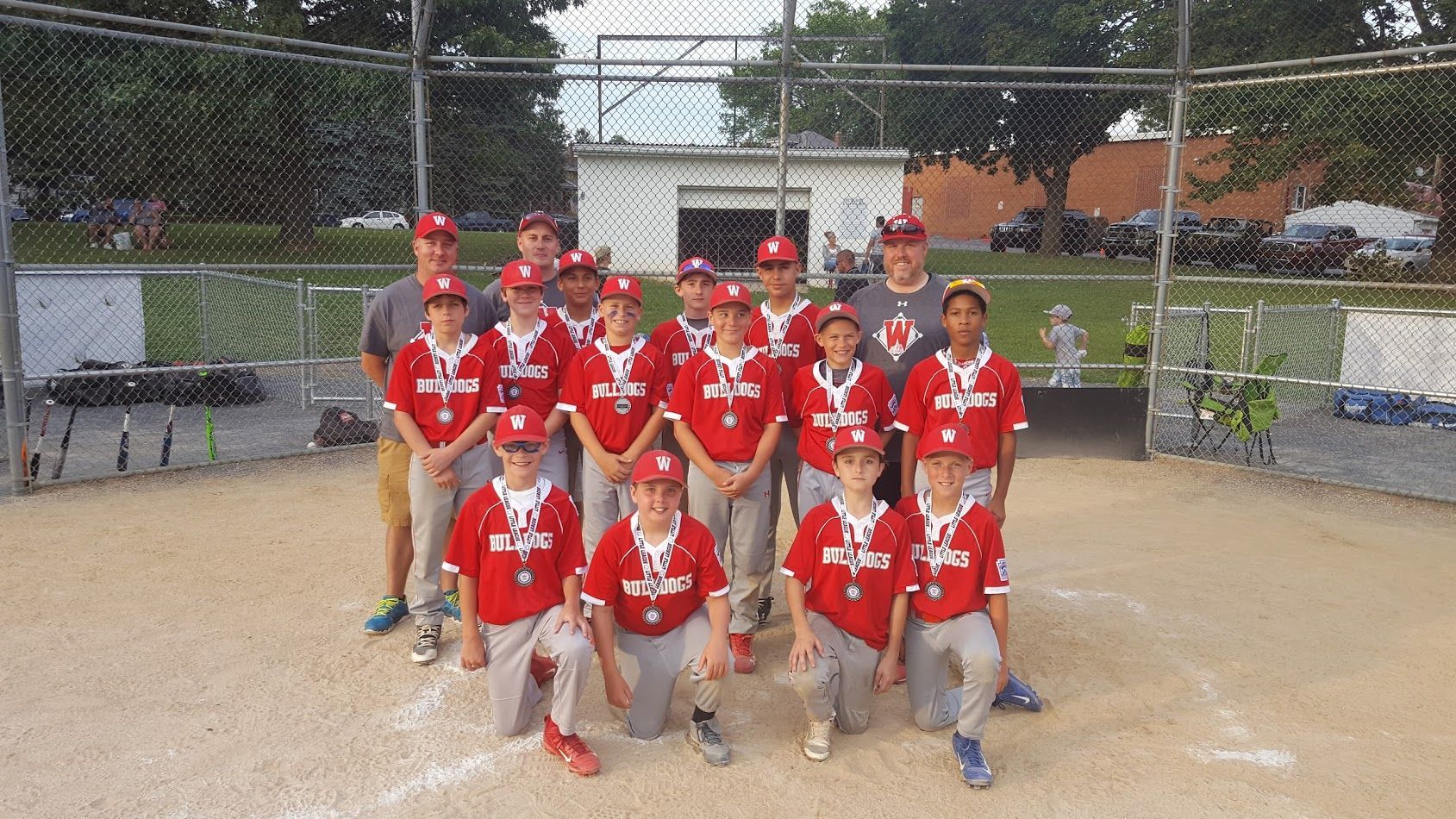 Youth baseball team in red uniforms posing on a field in front of a chain-link backstop