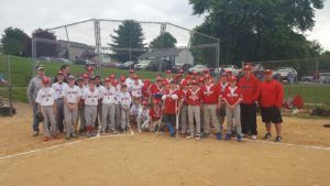 Youth baseball team posing on a dirt field, with players in white and red uniforms in front of a chain-link fence.