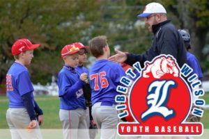 Youth baseball coach talks with players in blue uniforms and red caps on a field