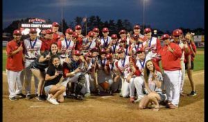 Baseball team in red and white uniforms posing together on a field at night after a game