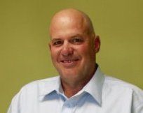 Smiling bald man in a light blue shirt against a green background