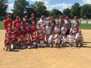 Baseball team posing on a dirt field, wearing red and white uniforms with red caps.
