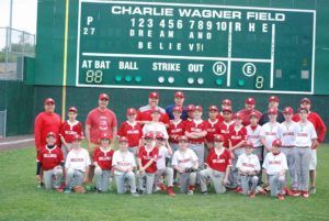 Youth baseball team posed in front of Charlie Wagner Field scoreboard, wearing red and white uniforms