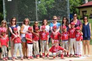 Youth baseball team posing with coaches in red uniforms at a ball field fence
