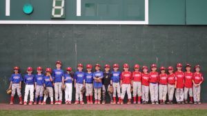 Two baseball teams in red and blue uniforms lined up on a field in front of a scoreboard