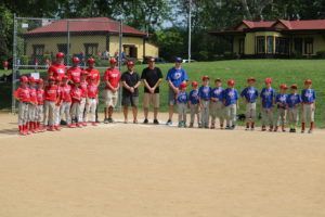 Two youth teams and coaches lined up on a cricket field, wearing red and blue uniforms.
