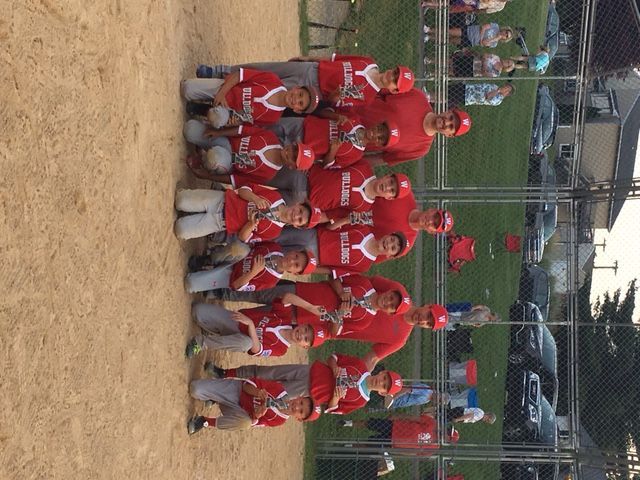 Youth baseball team in red uniforms posing on a dirt field with bats and helmets