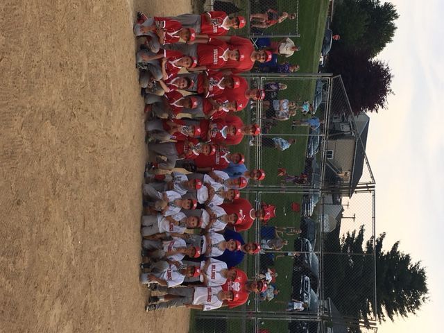 Youth sports team posing on a baseball field, with red and white uniforms and a backstop behind them