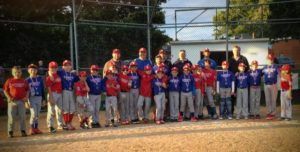 Youth baseball team posing on a field in red and blue uniforms during sunset
