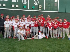 Youth baseball team in red jerseys posing on a baseball field in front of a scoreboard