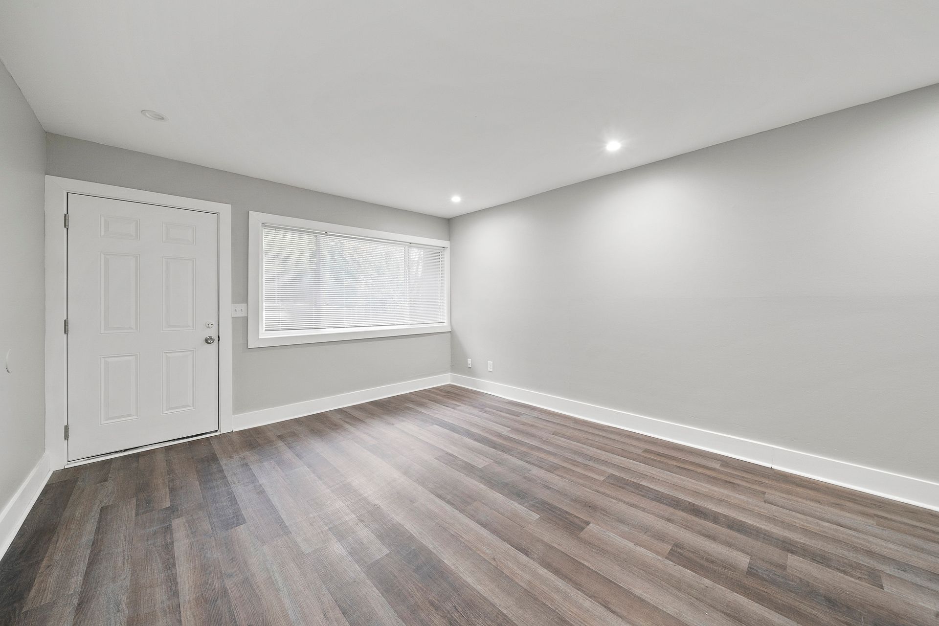 Empty gray bedroom with wood floors, white trim, window blinds, and a closet door